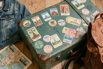 Valise vintage recouverte d'autocollants de voyage colorés posée sur un plancher en bois, entourée d'accessoires de road trip