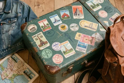 Valise vintage recouverte d'autocollants de voyage colorés posée sur un plancher en bois, entourée d'accessoires de road trip